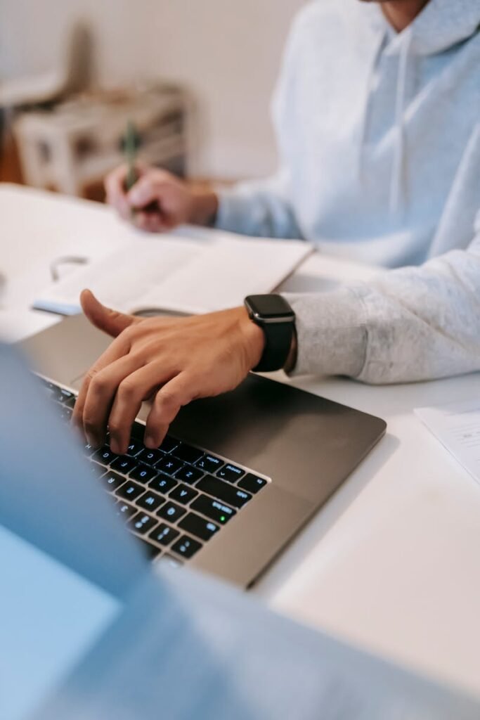 pexels-photo-6393010-6393010 From above of crop unrecognizable freelancer in casual clothes sitting at table with notebook and working on netbook in light room